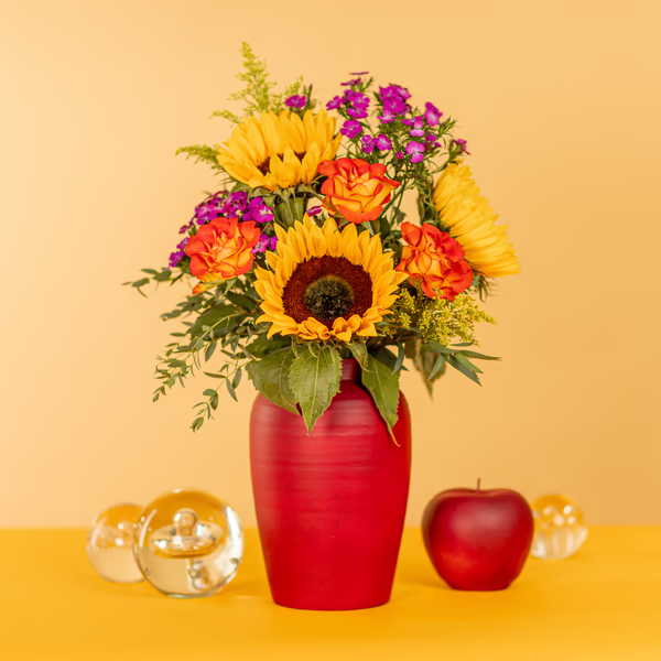 A sunflower bouquet with roses in a red vase